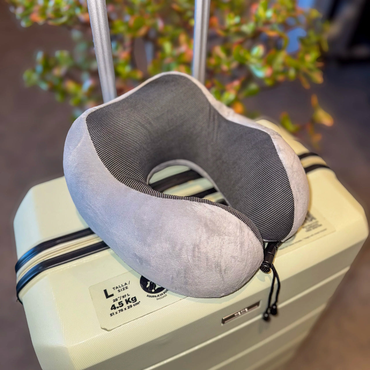 Coussin cervical ergonomique en velours gris perle posé sur une valise. Parfait pour le confort lors des voyages grâce à sa mousse à mémoire de forme, pratique et portable.