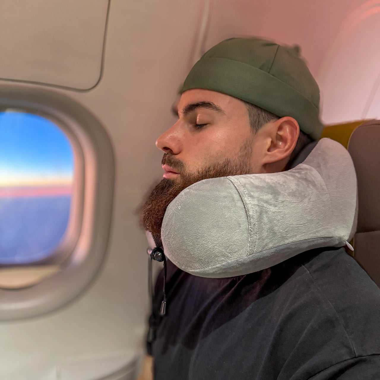 Voyageur en avion reposant avec un coussin cervical ergonomique en velours gris perle. Idéal pour un maintien confortable du cou grâce à la mousse à mémoire de forme, parfait pour les longs trajets.