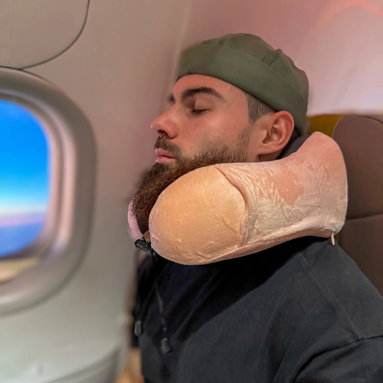 Homme utilisant un coussin de voyage en velours rose avec mousse à mémoire de forme, idéal pour un confort optimal lors des trajets en avion.