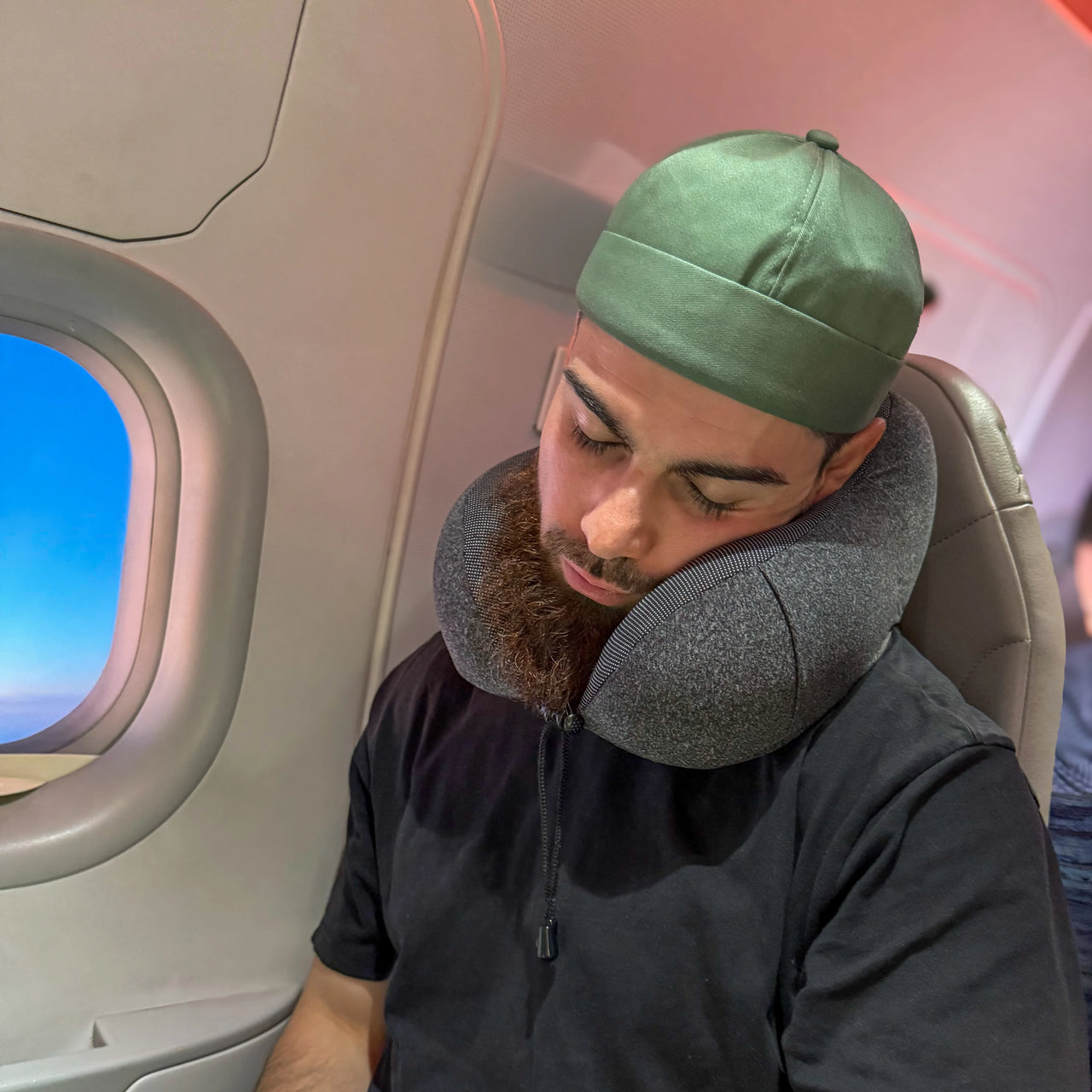 Personne utilisant un coussin de voyage ergonomique couleur anthracite dans un avion. Conçu pour un soutien cervical optimal et un confort supérieur en déplacement.