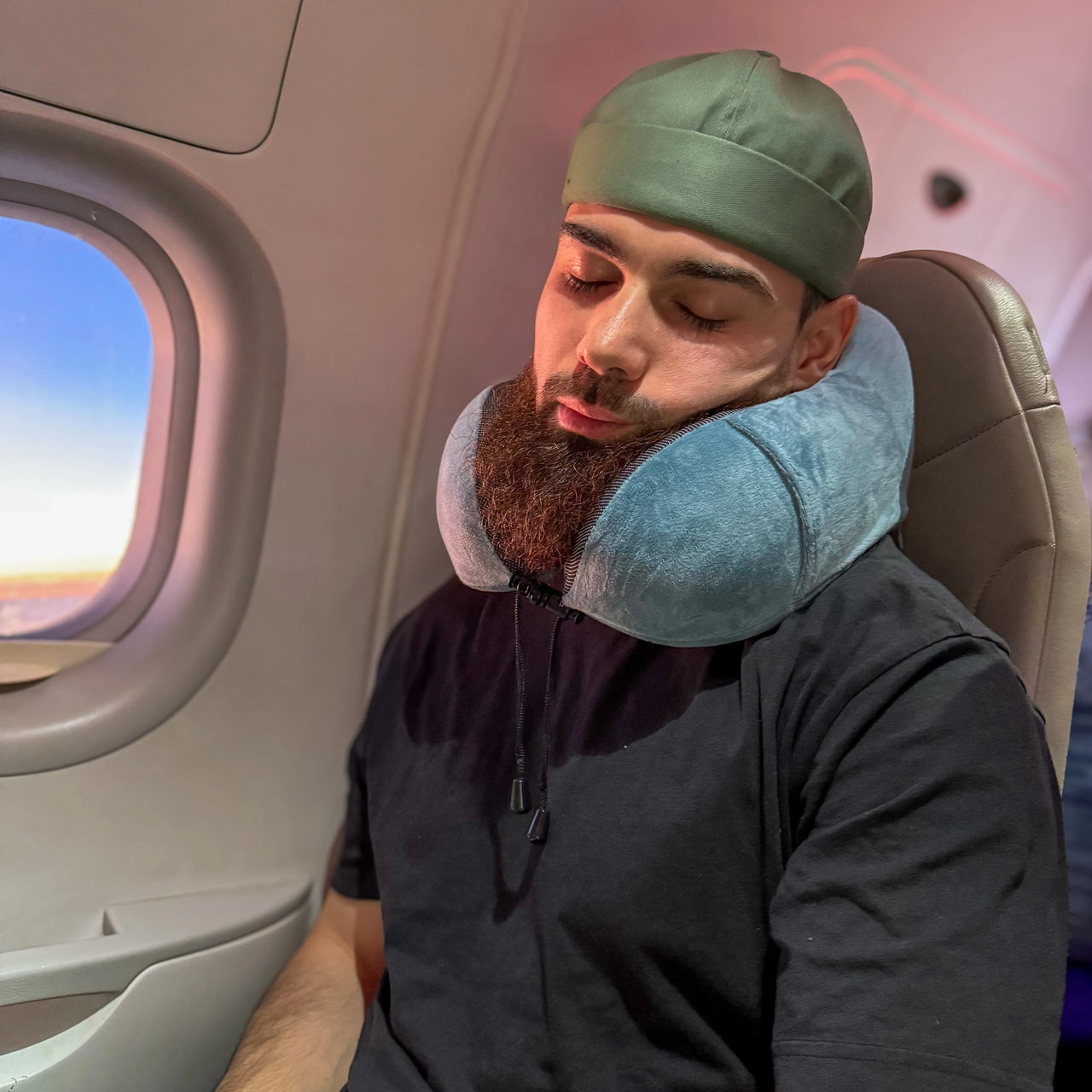 Personne utilisant un coussin de voyage à mémoire de forme bleu dans un avion. Accessoire ergonomique et confortable pour soutenir le cou pendant les trajets aériens.