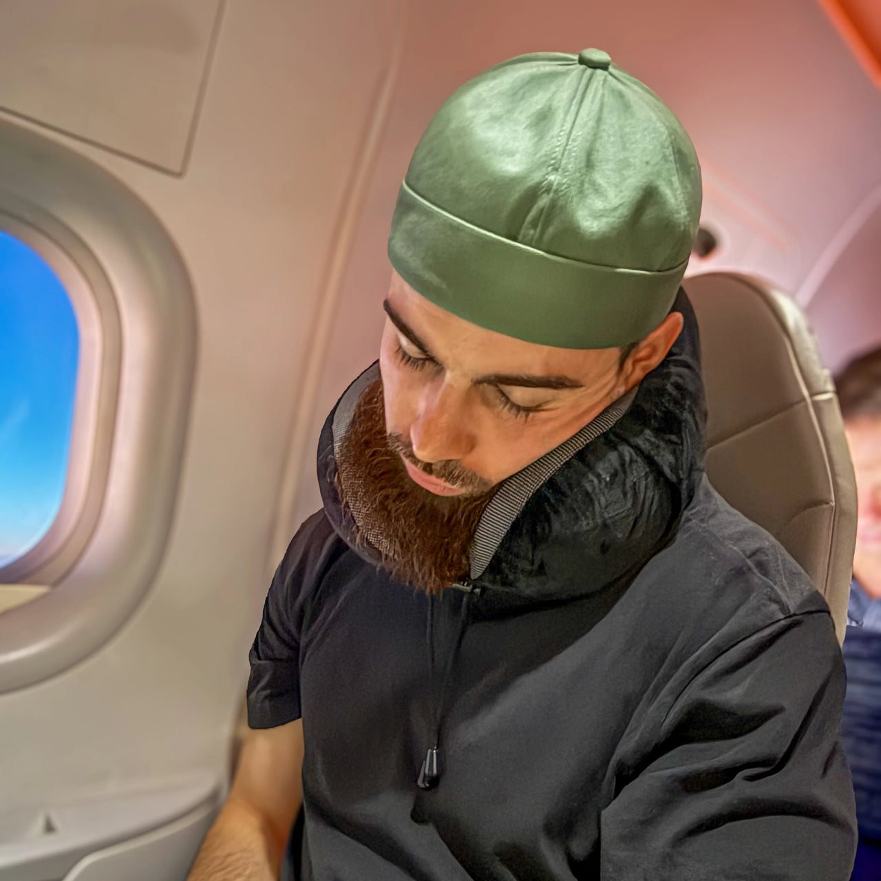 Personne utilisant un coussin de voyage ergonomique noir dans un avion. Accessoire idéal pour un soutien cervical et un confort optimal lors des déplacements.