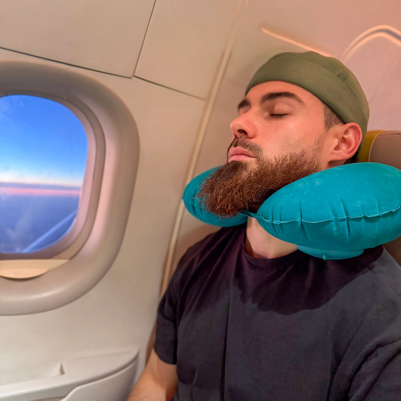 Homme utilisant un coussin de voyage gonflable bleu autour du cou pour un soutien ergonomique et un confort optimal pendant un vol en avion.