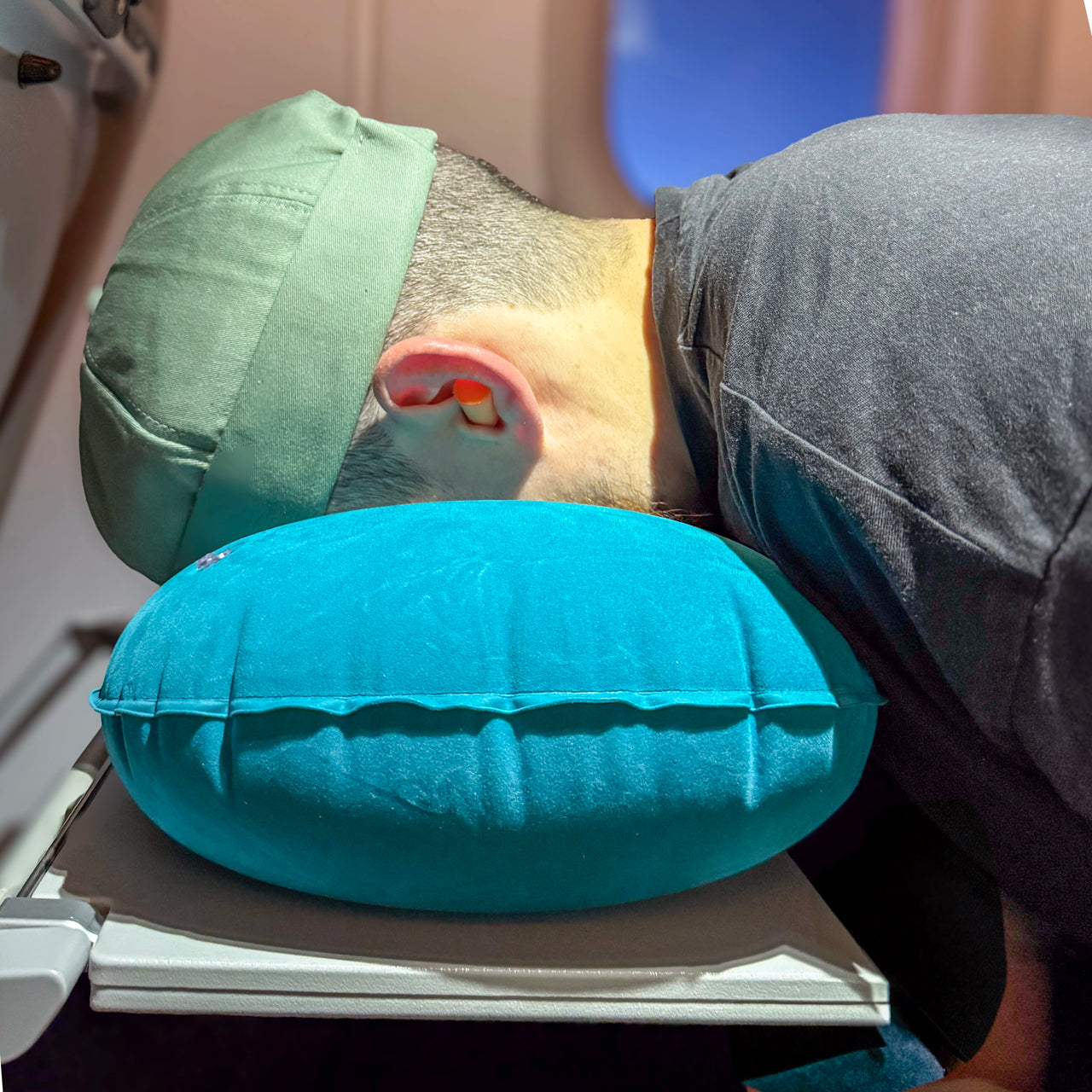 Homme reposant son visage sur un coussin de voyage gonflable bleu pendant un vol en avion, offrant un soutien ergonomique et un confort optimal pour les trajets.