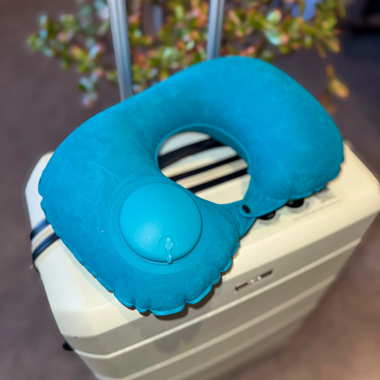 Coussin de voyage gonflable bleu posé sur une valise, équipé d'un système de pompe intégré pour un gonflage rapide. Accessoire compact et pratique pour voyager.