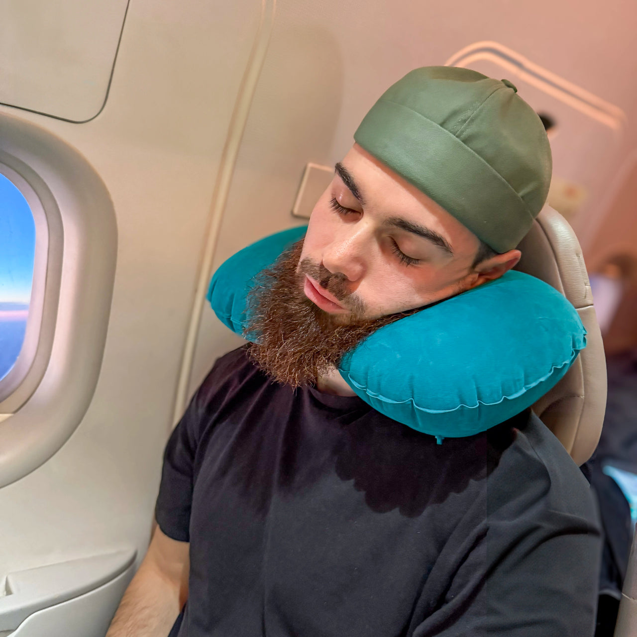 Homme utilisant un coussin de voyage gonflable bleu pour un soutien ergonomique du cou pendant un vol en avion. Accessoire idéal pour voyager confortablement.