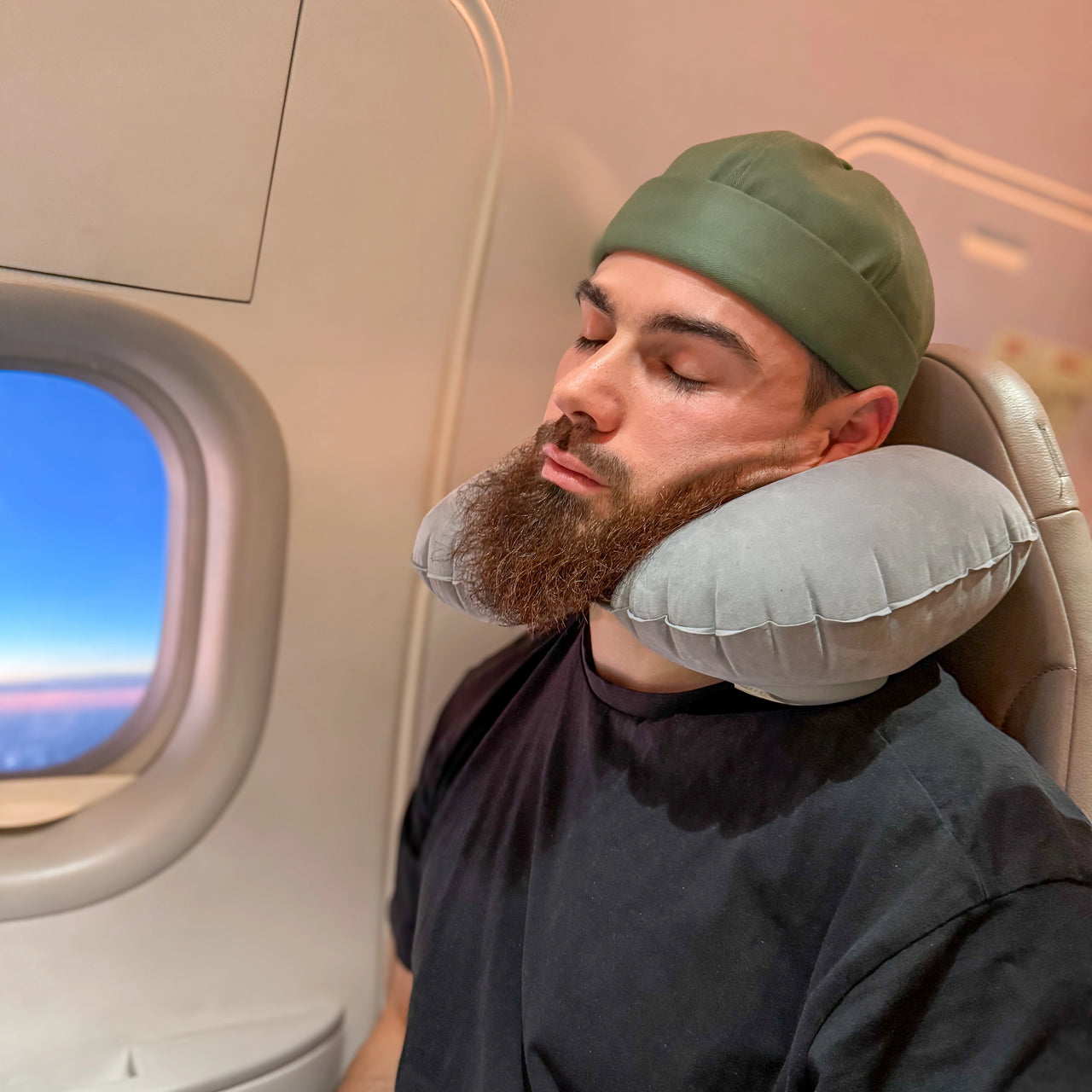 Homme utilisant un coussin de voyage gonflable gris pour un soutien ergonomique du cou pendant un vol en avion. Confort idéal pour les longs trajets.