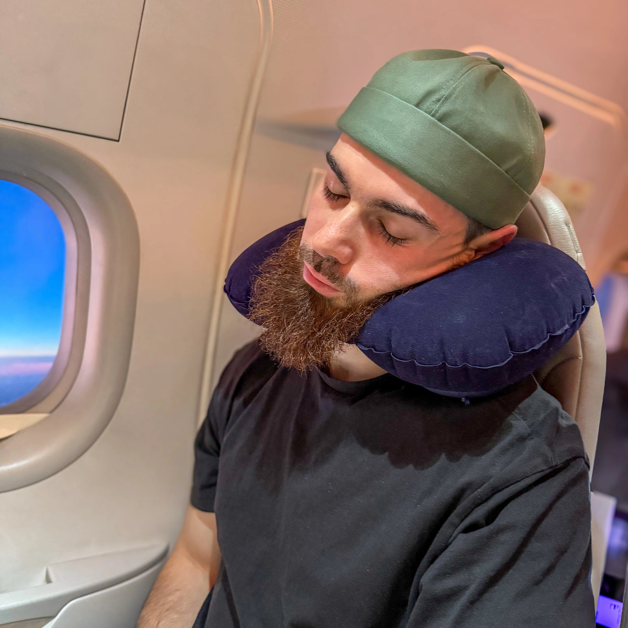 Homme utilisant un coussin de voyage gonflable bleu marine pour un soutien ergonomique du cou pendant un vol en avion. Idéal pour voyager confortablement et léger.