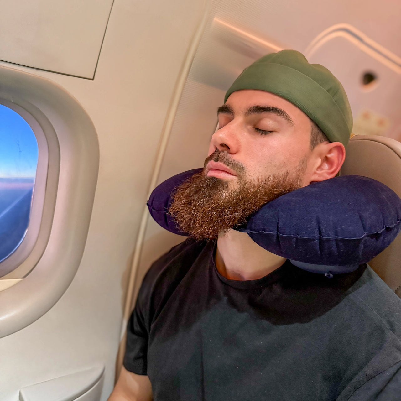 Homme utilisant un coussin de voyage gonflable bleu marine pour un soutien ergonomique du cou pendant un vol en avion. Confort idéal pour les trajets longs.