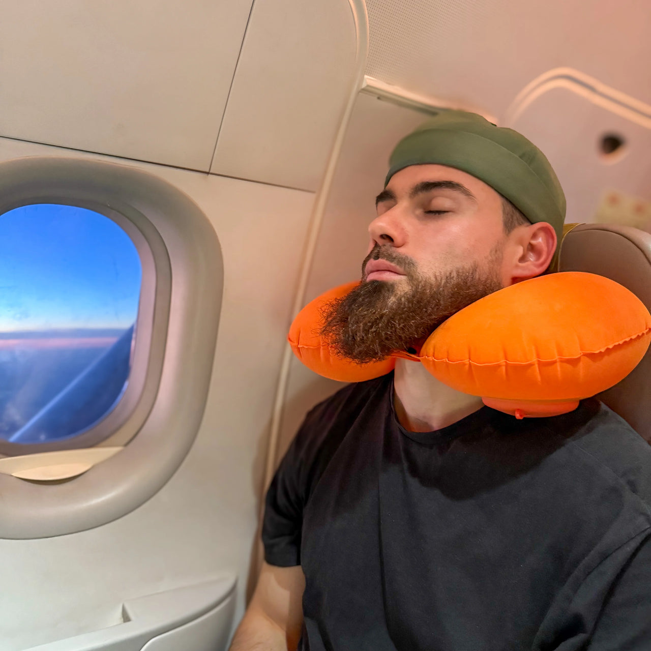 Homme utilisant un coussin de voyage gonflable orange autour du cou pendant un vol en avion. Accessoire confortable et ergonomique pour des trajets relaxants.