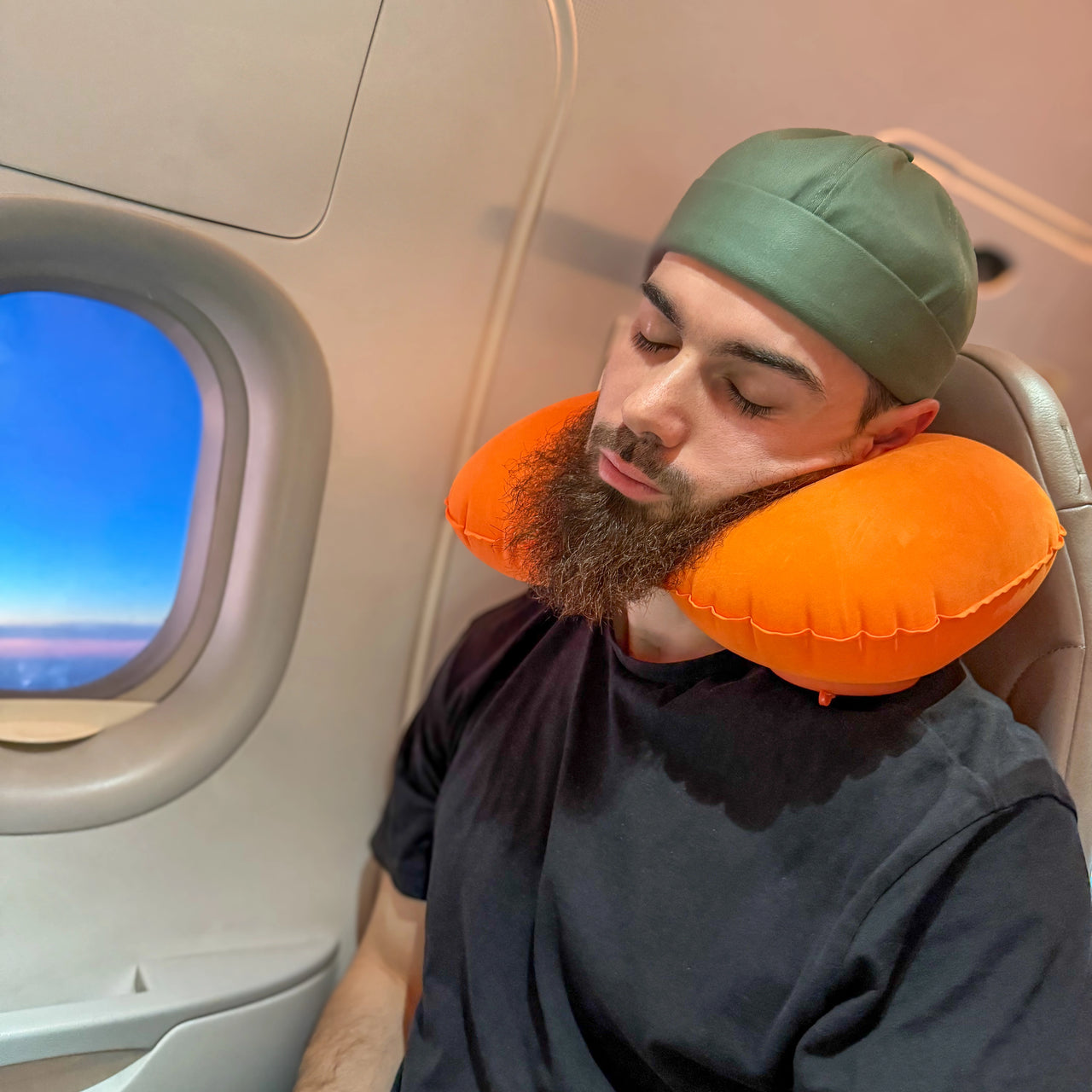 Homme utilisant un coussin de voyage gonflable orange pour un soutien ergonomique du cou pendant un vol en avion. Accessoire léger et pratique pour voyager confortablement.