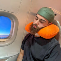 Thumbnail for Homme utilisant un coussin de voyage gonflable orange pour un soutien ergonomique du cou pendant un vol en avion. Accessoire léger et pratique pour voyager confortablement.