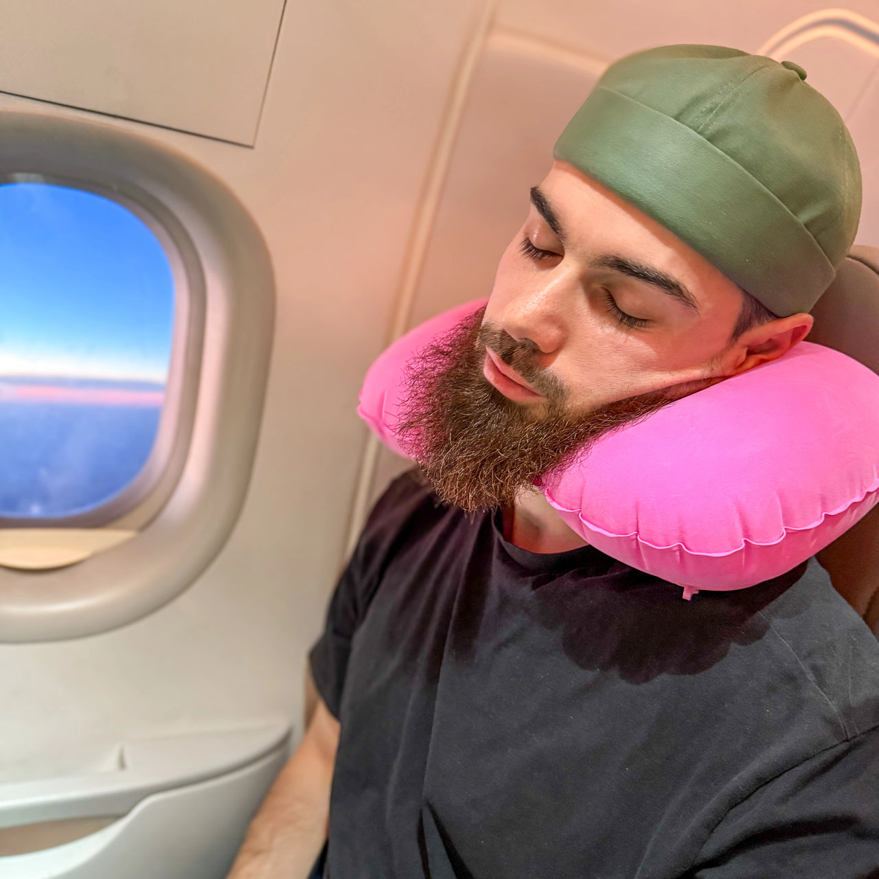 Homme utilisant un coussin de voyage gonflable rose pour un soutien ergonomique du cou pendant un vol en avion. Accessoire léger et pratique pour les voyages.