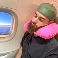 Thumbnail for Homme utilisant un coussin de voyage gonflable rose pour un soutien ergonomique du cou pendant un vol en avion. Accessoire léger et pratique pour les voyages.