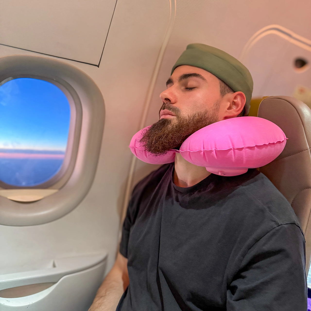 Voyageur endormi confortablement avec un coussin de voyage gonflable rose, idéal pour soutenir la tête et le cou pendant un vol en avion. Confort et légèreté pour les longs trajets.