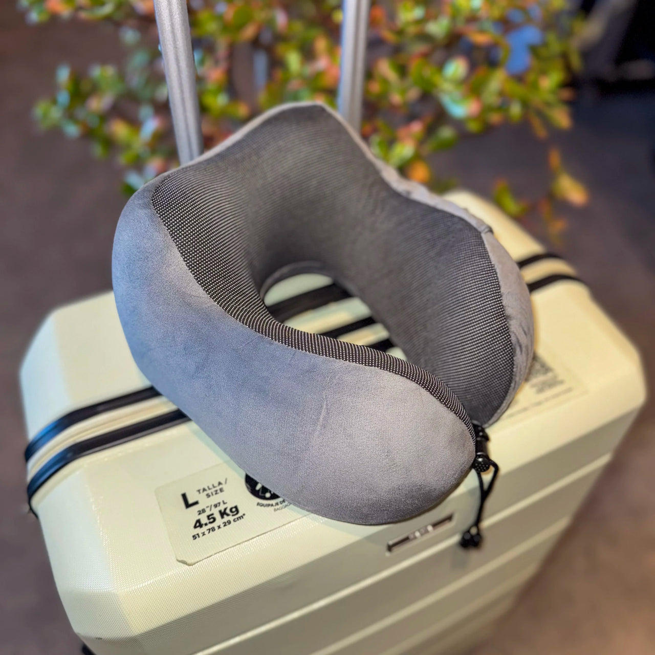 Coussin de voyage en velours gris anthracite posé sur une valise. Confortable, ergonomique, et équipé de mousse à mémoire de forme pour un soutien optimal lors de vos déplacements.