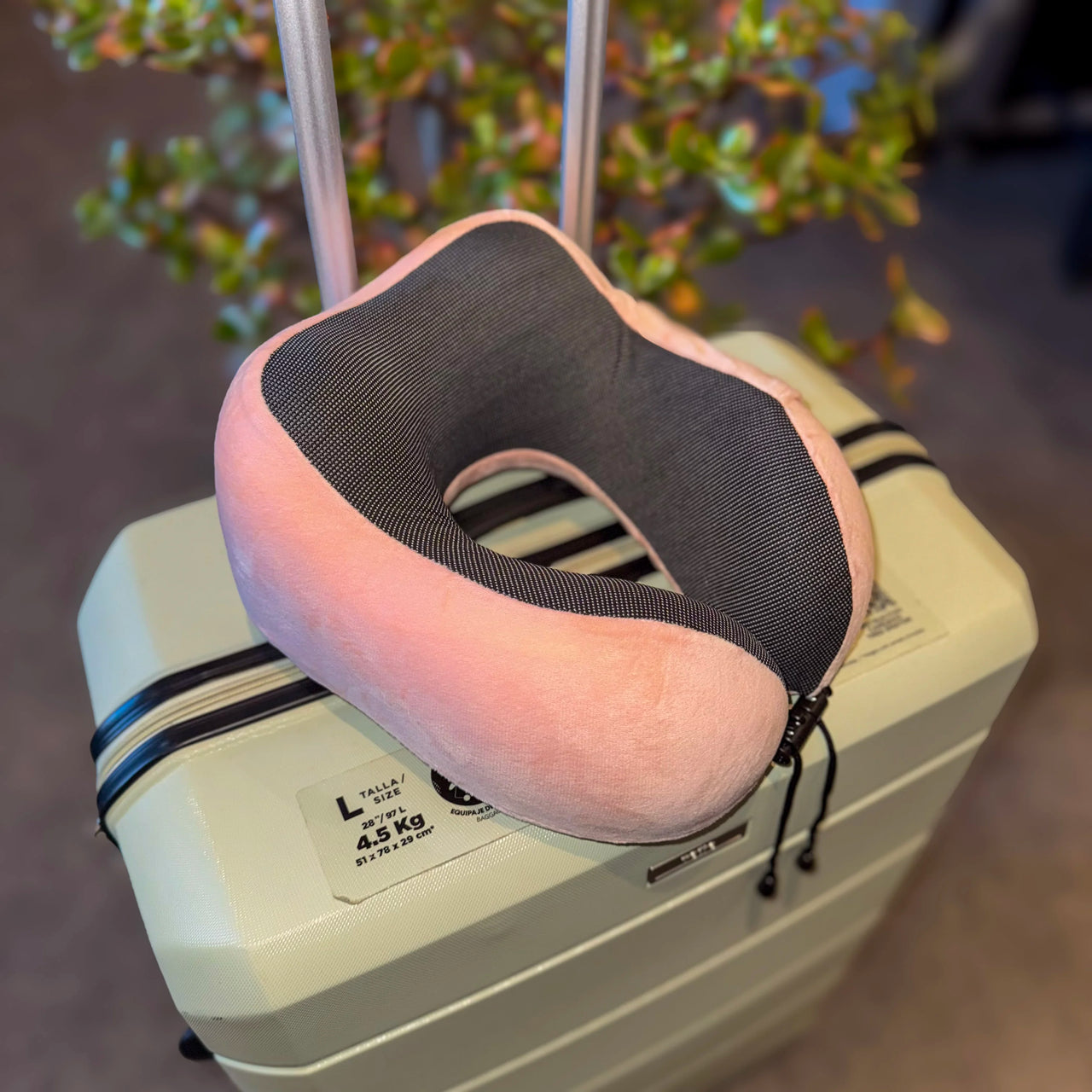 Oreiller de voyage en velours rose posé sur une valise, parfait pour des trajets confortables grâce à sa mousse à mémoire de forme et son design ergonomique.